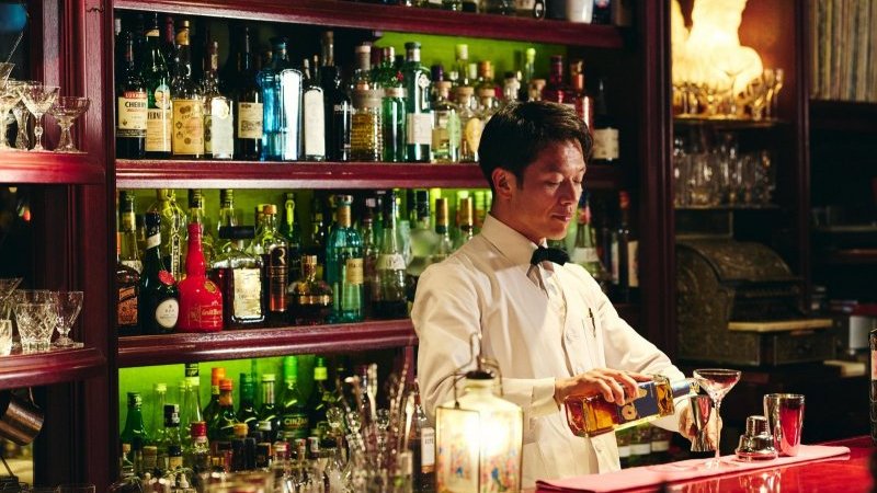 バーカウンターの後ろにひげを生やしたハンサムな若いバーテンダー。かっこいい腕時計。Premium写真